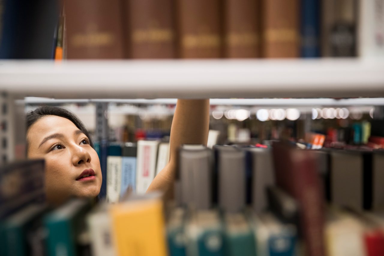 Student looking through library book shelves